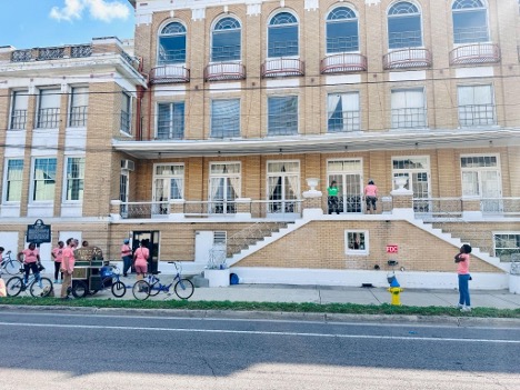 People in pink and green shorts with bicycles in front of building