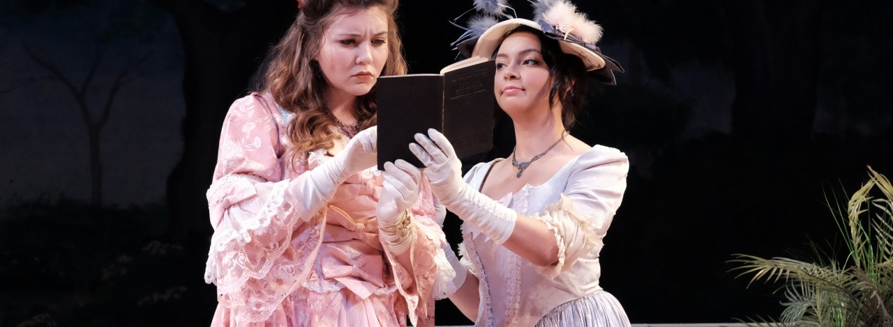 Two actresses in vintage costumes reading a book together