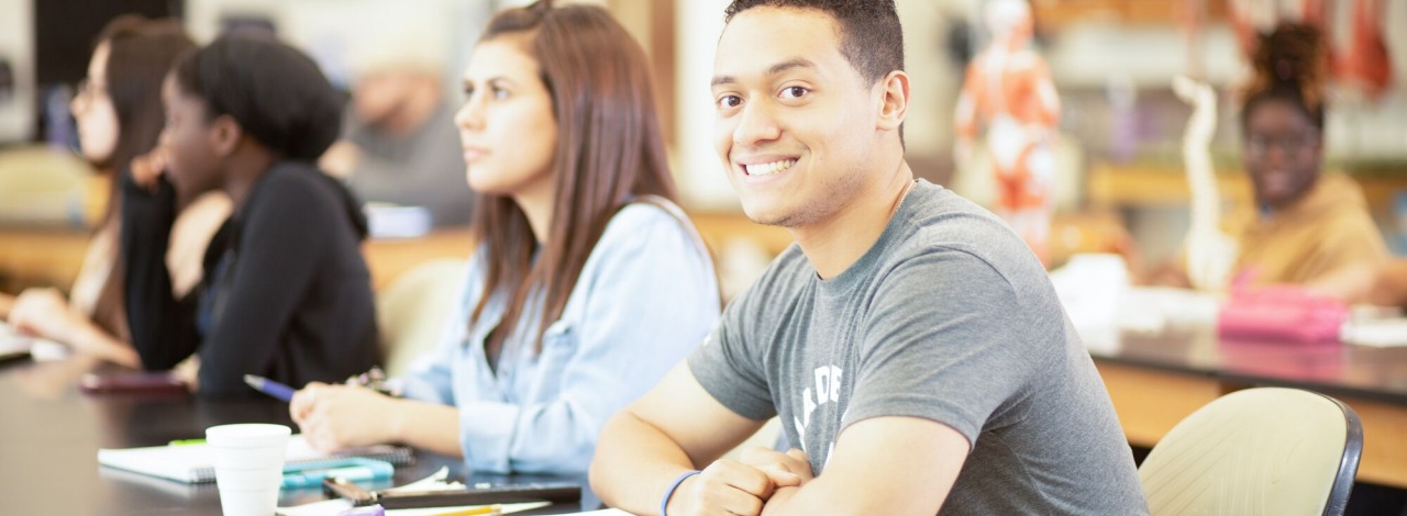 Latino male smiling in a classroom with other students during a lecture