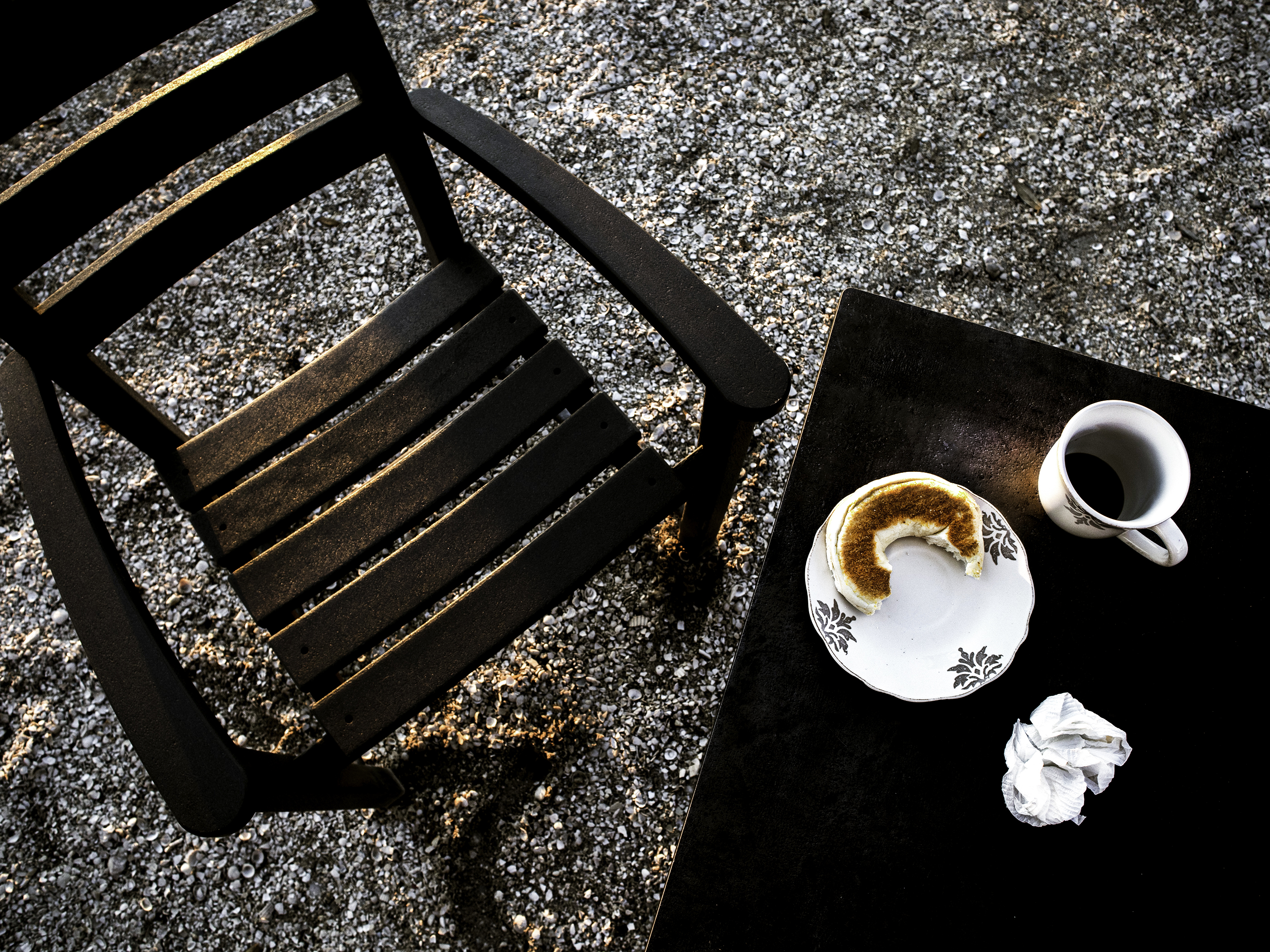 Table and chair seen from above with coffee, bagel, and crumpled napkin