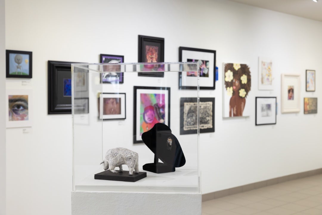 Clear acrylic box containing a sculpture of a bul and jewelry with paings on wall in background