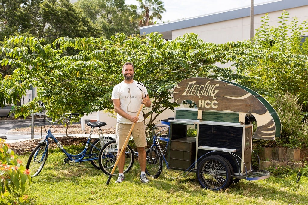 Man holding rake standing in front of bicycle pulling cart