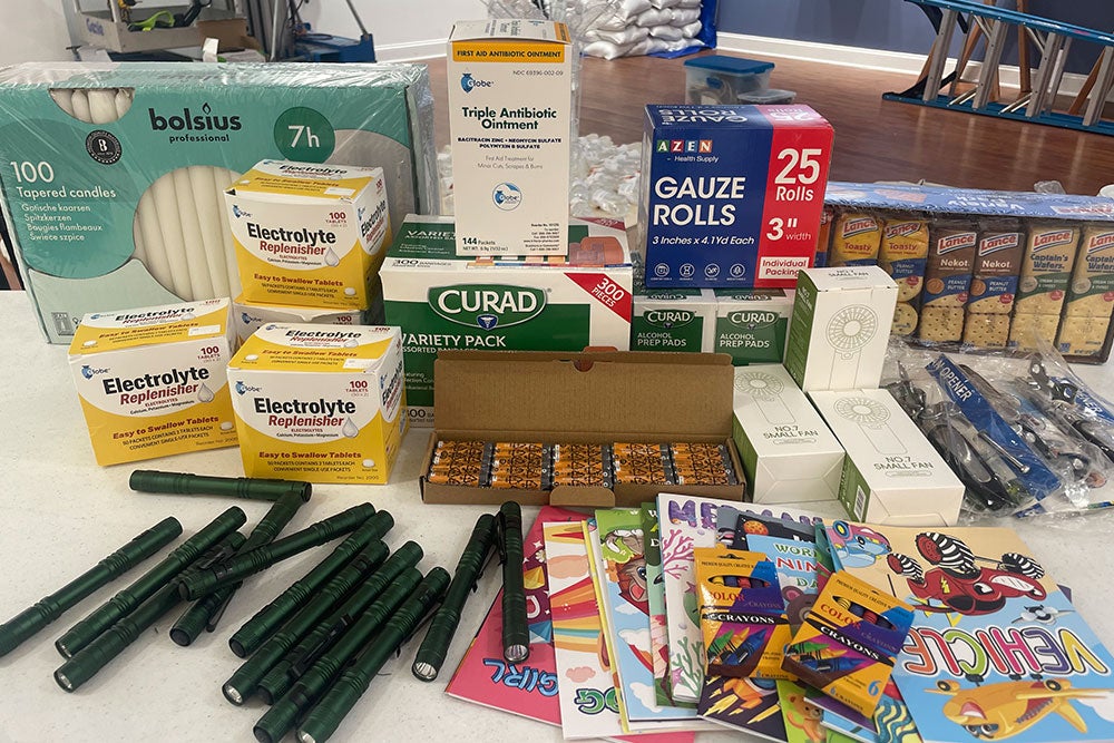 Various medical and personal supplies on a table, including candles, electrolyte tablets, gum, bandages, ointment, gauze, crackers, and children’s books with crayons.