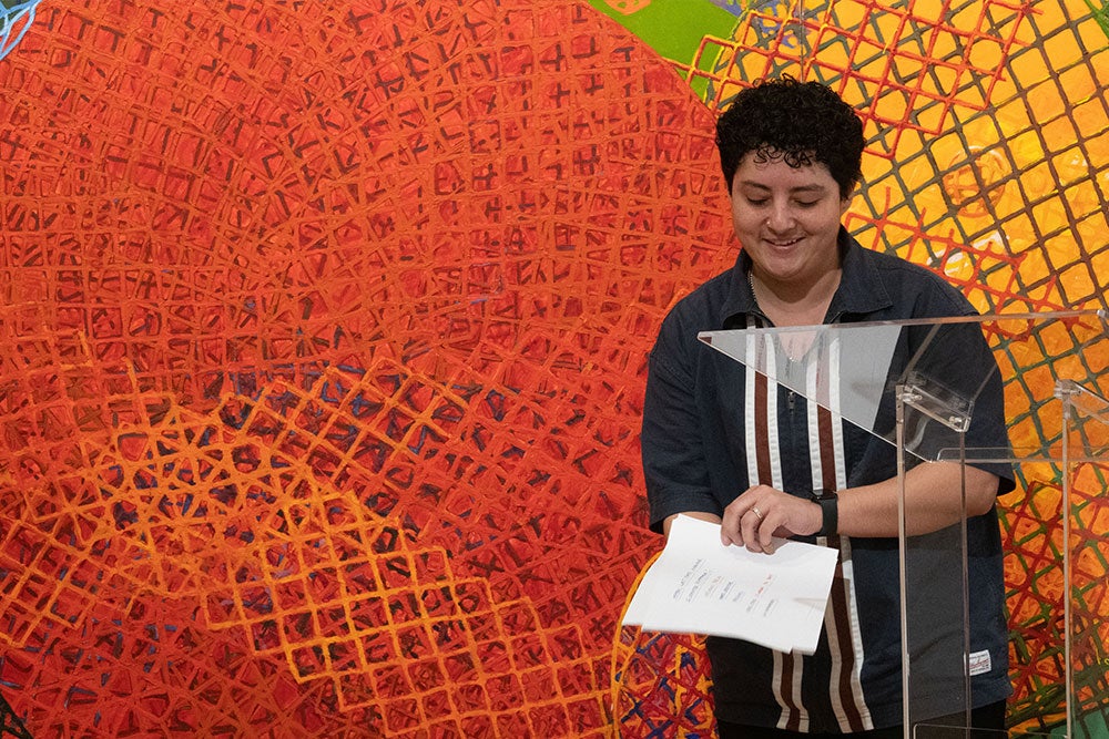 Person smiling beside a podium with abstract artwork in the background.