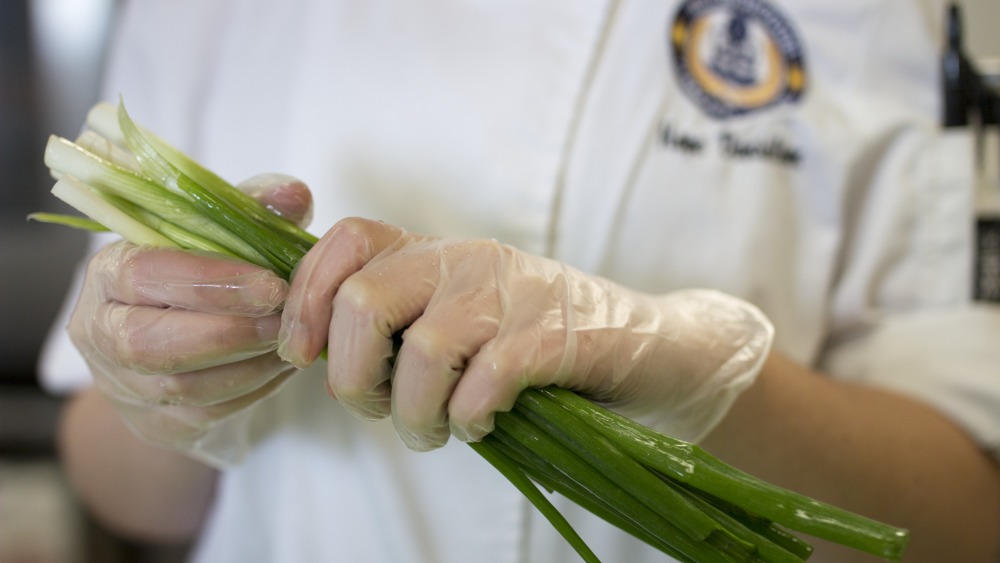 closeup of hands holding washed green onions, individual is wearing a chef's jacket with the HCC seal