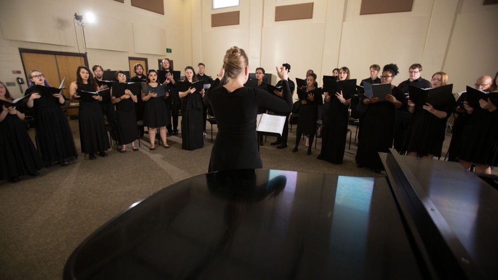Backside of a choir conductor orchestrated a group of choir students, all wearing black