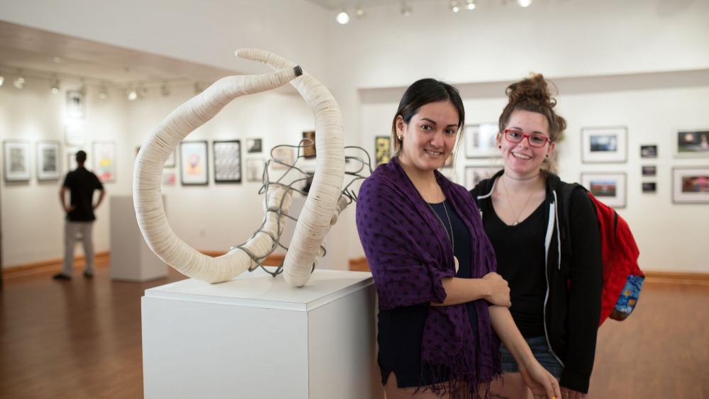Two young females smiling and posing inside the Ybor City campus art gallery