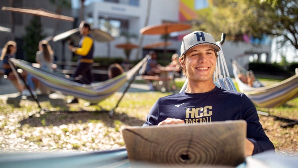 Male student sitting in a hammock with a laptop in his lap. 