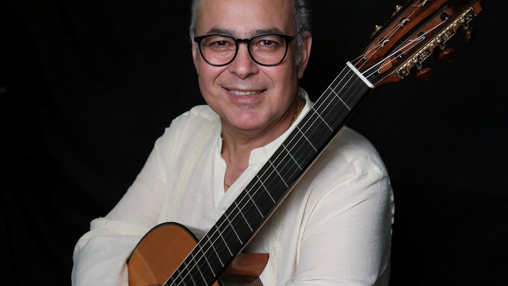 Rafael Martín Padrón smiling with a classical guitar against a dark background.