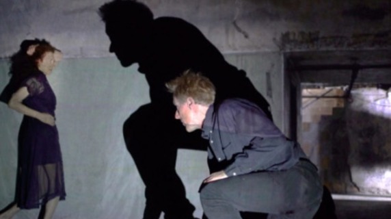 Man squatting; his dark shadow appears to talk with woman