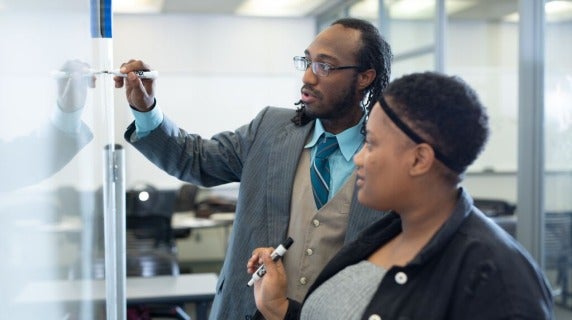 Faculty member helping student with a whiteboard problem.