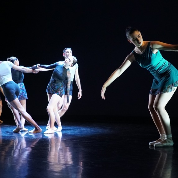 A group of dancers in a circle in /the background with a single dancer in the foreground