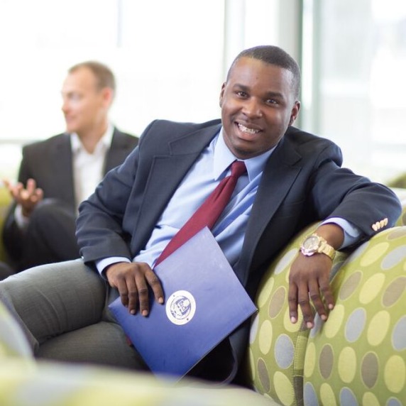 smiling, African-American male in a business suit sitting casually on a couch with other business professionals