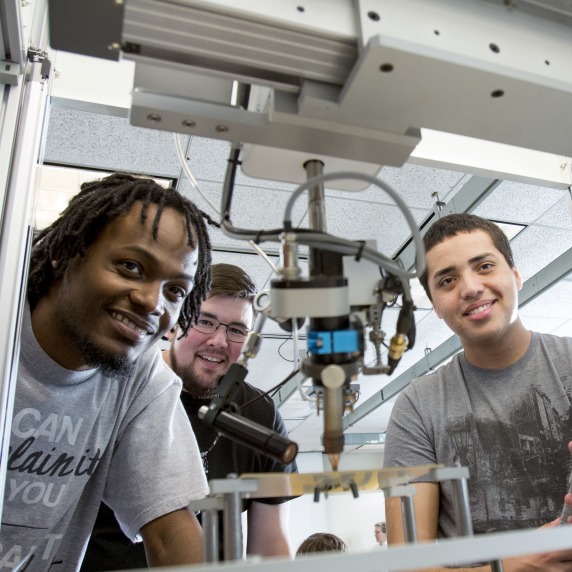 Engineering students looking through 3D printing machine