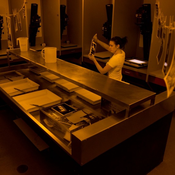 Overhead look at a photo student working in a darkroom with the amber lights on 