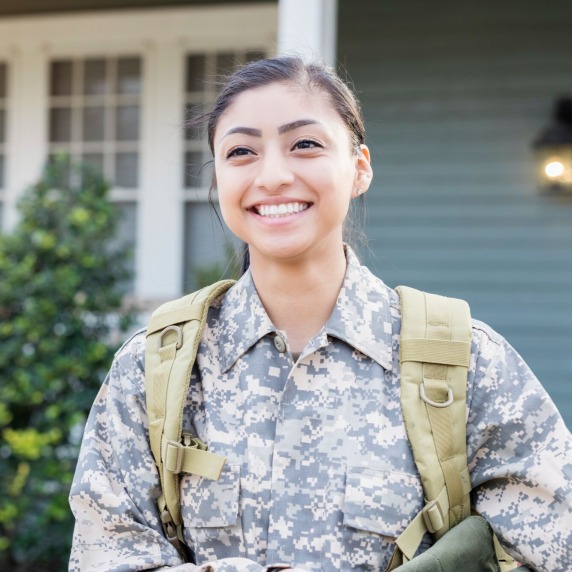 Happy young Hispanic female soldier is excited for her first deployment. Her house is in the background as she walks away.