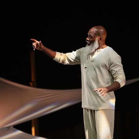 A man standing in ragged gray sweats reaching out with one arm