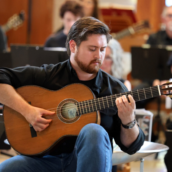 Photo of Kenneth Bender seated playing guitar