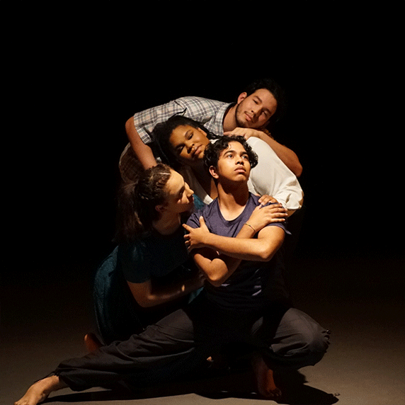 Four people in an intertwined pose on a dark stage