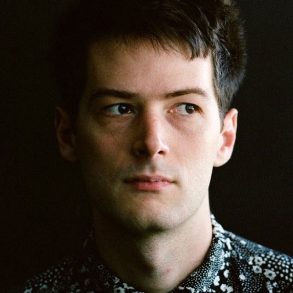 A man with short hair in a floral shirt, standing against a neutral background.