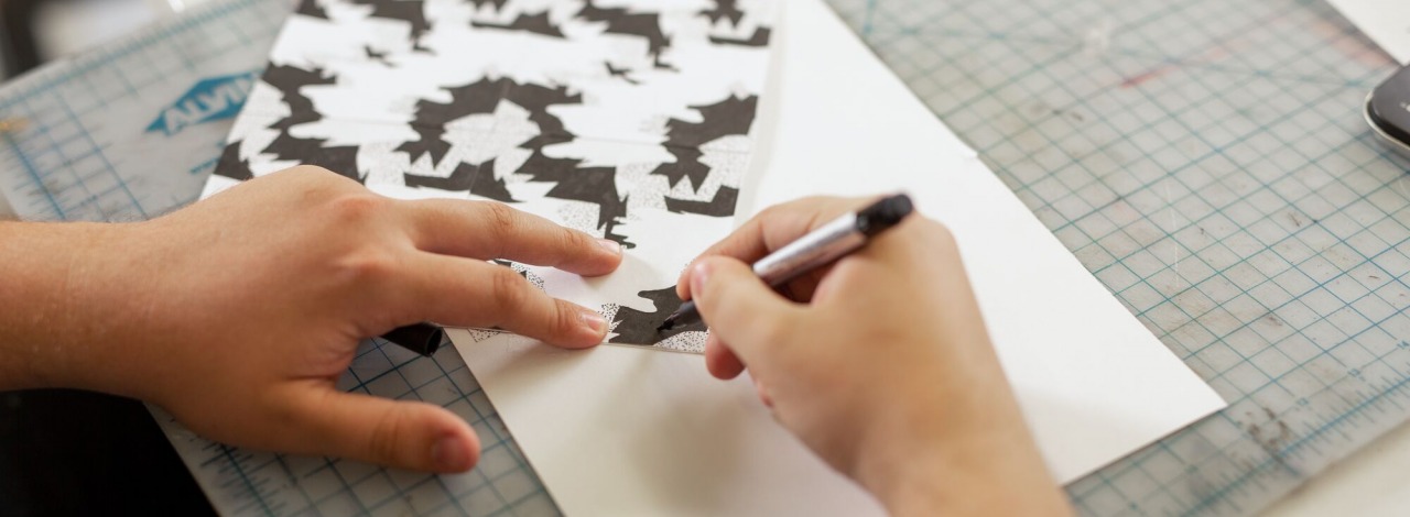 close-up of hands drawing a tessellation on paper pressed on a self-healing cutting mat