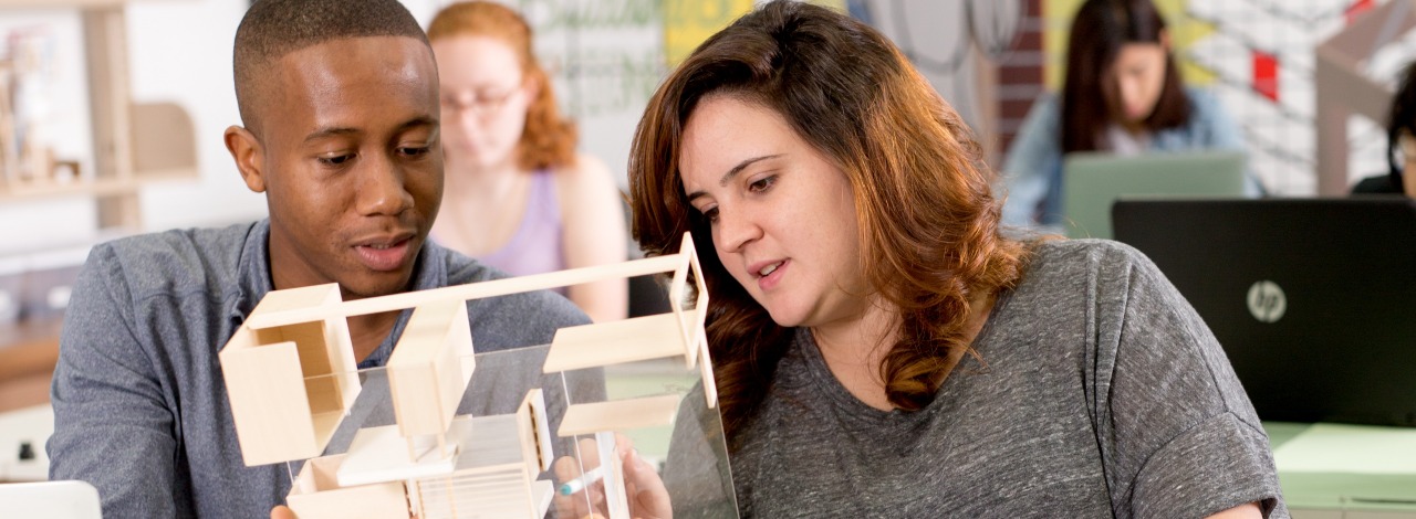 two students looking at a wooden architectural model together in a classroom