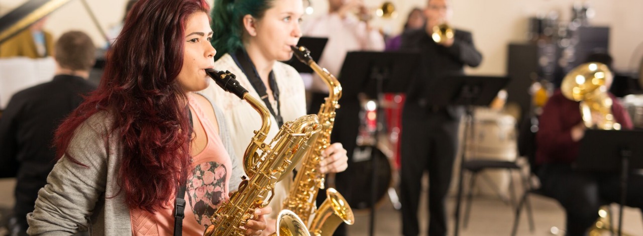 Two female students playing the saxophone with the rest of the HCC Jazz Band behind them