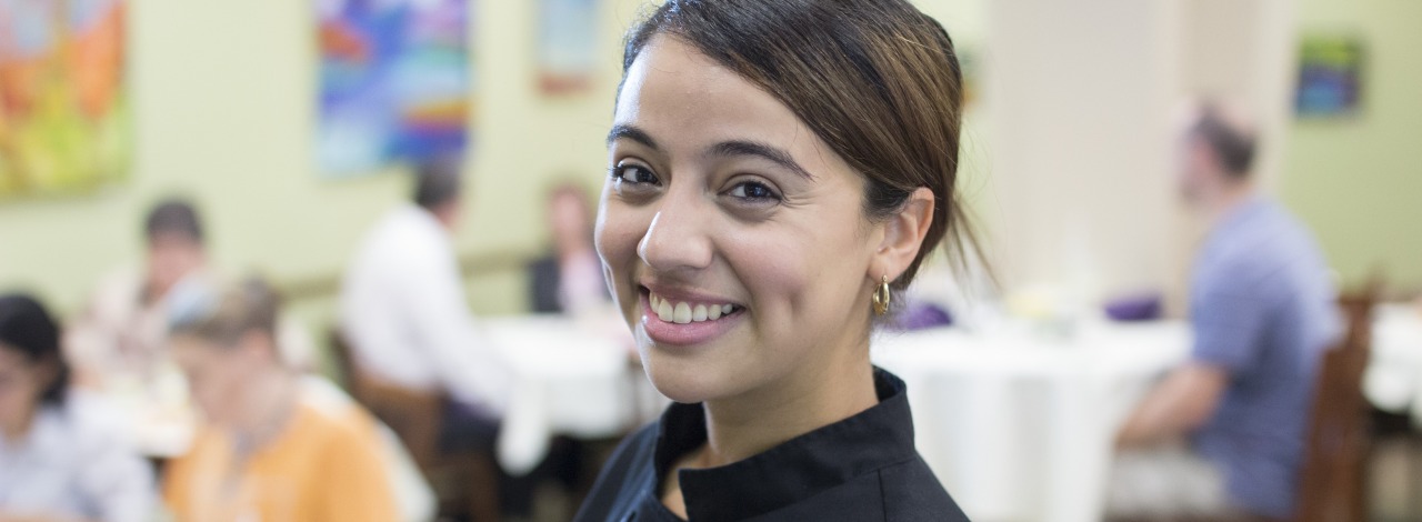 Female student smiling, wearing a black chef jacket with the HCC seal on embroidered on it