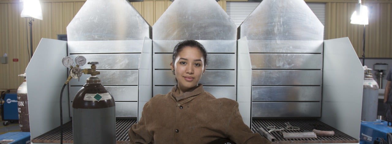 Female welding student in leather coverall holding helmet