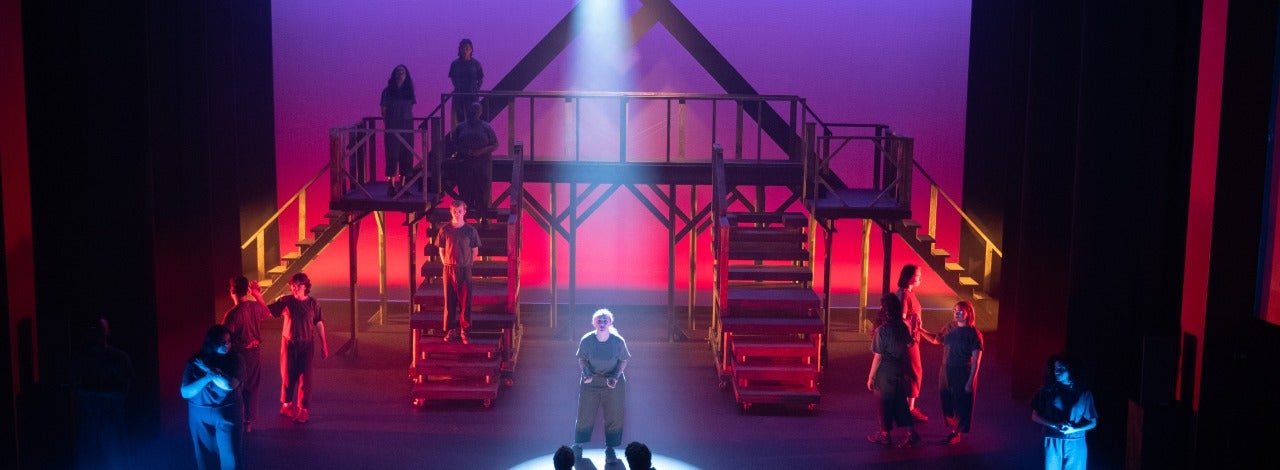 Two people seated watching a person onstage with outstretched hands