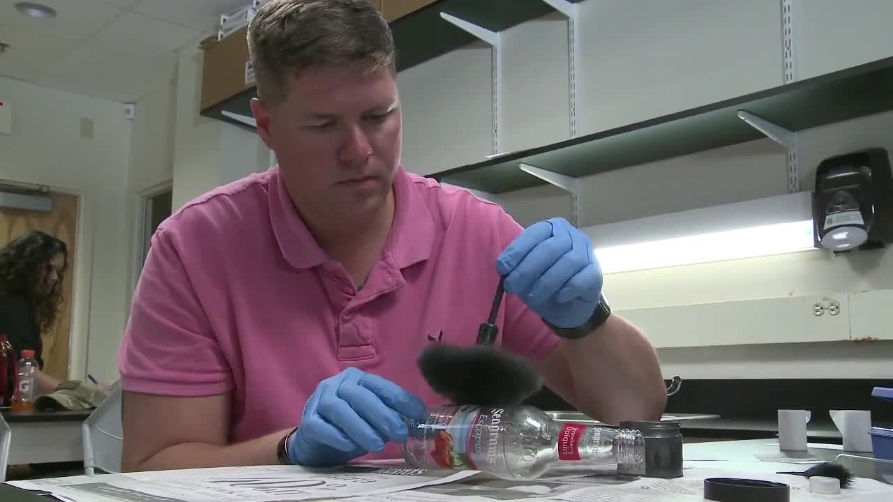 man dusting for prints on bottle