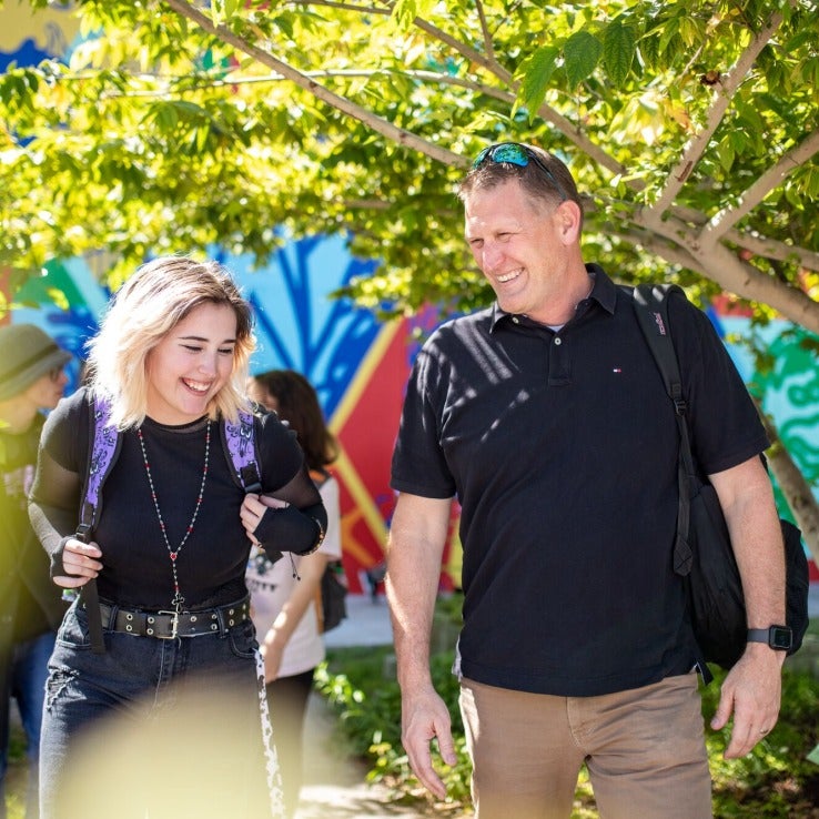 Two people walking and smiling through a garden on campus. 