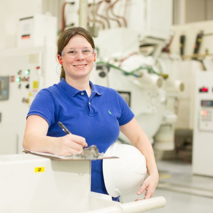 Woman holding hardhat in front of industrial equipment