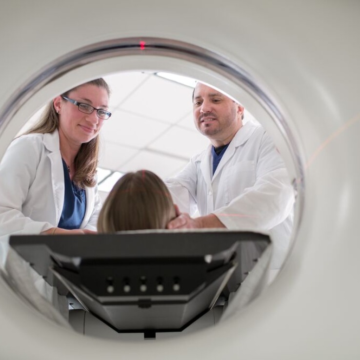 A man and woman in lab clothes help a patient in a CT machine