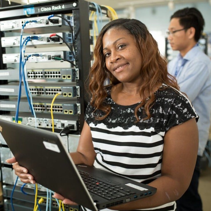 Woman with laptop in front of networking equipment