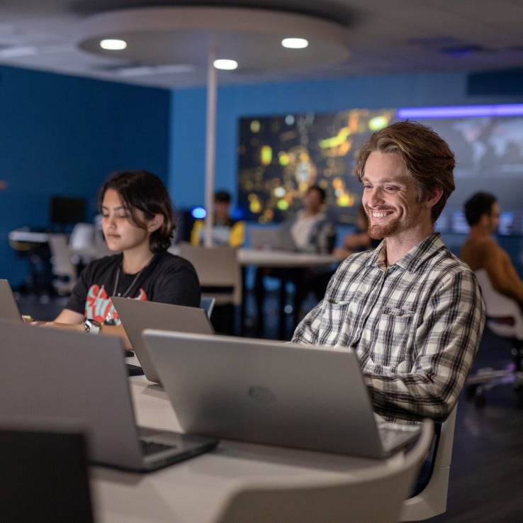 Two students sitting in a classroom working on laptops.