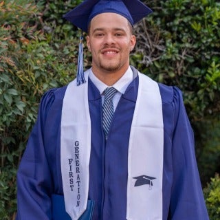 Man dressed in blue cap and gown with white sash